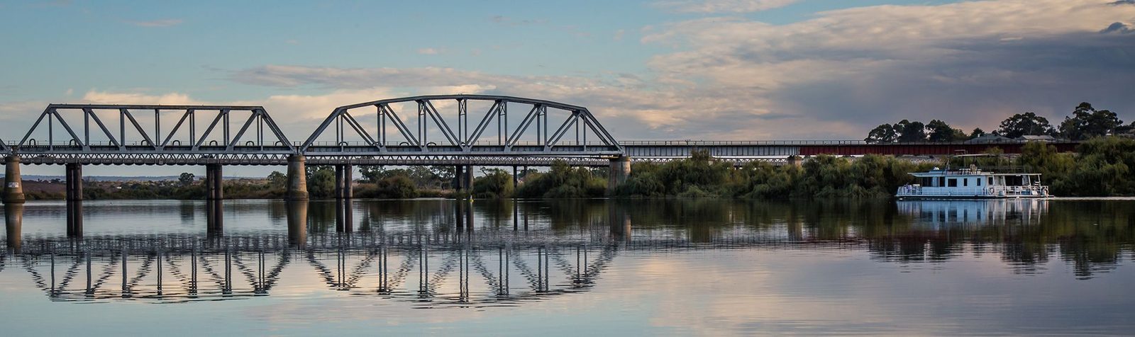 The Murray Bridge road bridge reflected in a still river at dusk, a houseboat moored nearby